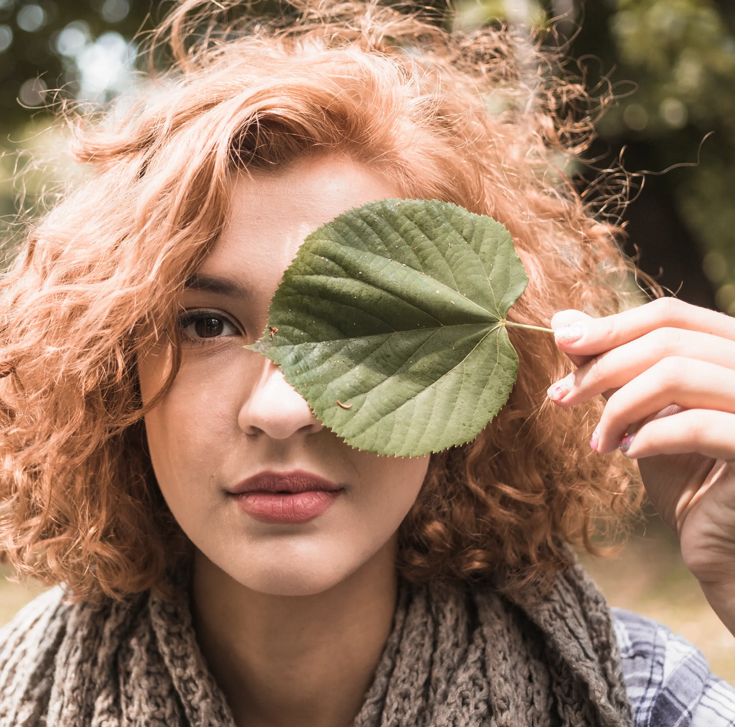 Młoda kobieta trzymająca zielony liść w dłoni – symbol troski o naturę i postaw proekologicznych.